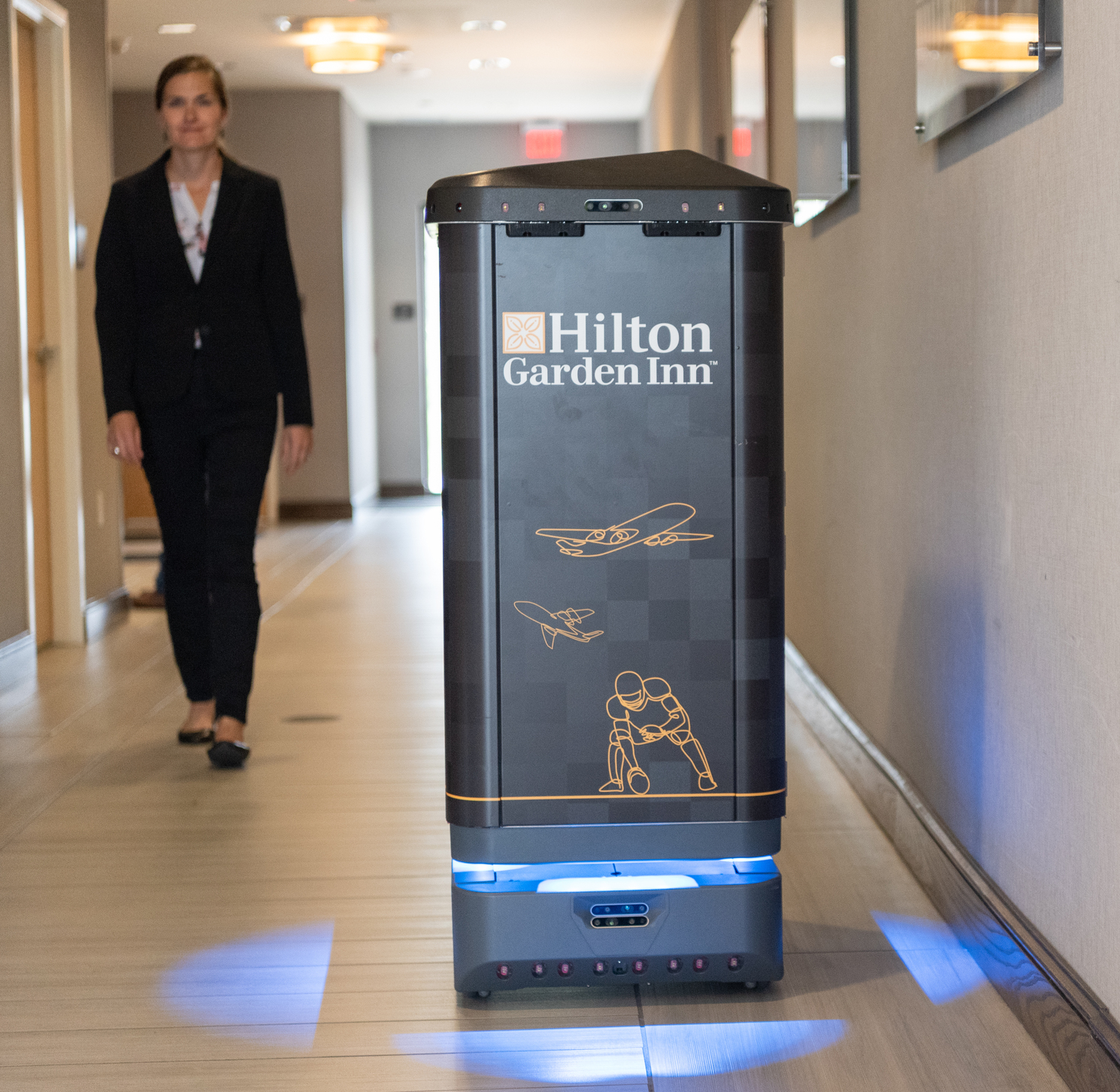 hotel delivery robot navigating hallway while guest walks by