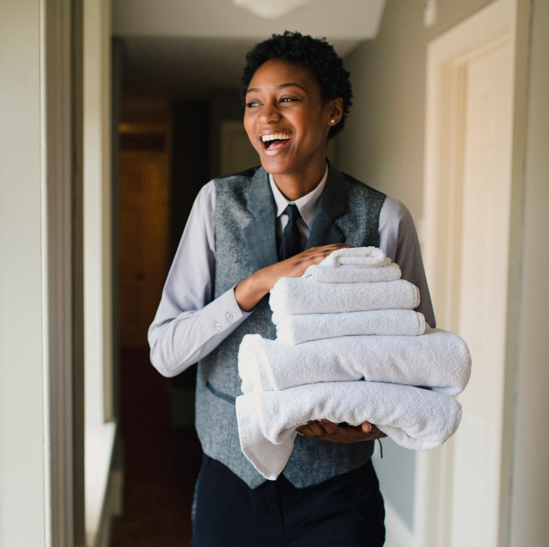hotel housekeeper smiling while holding a stack of towels